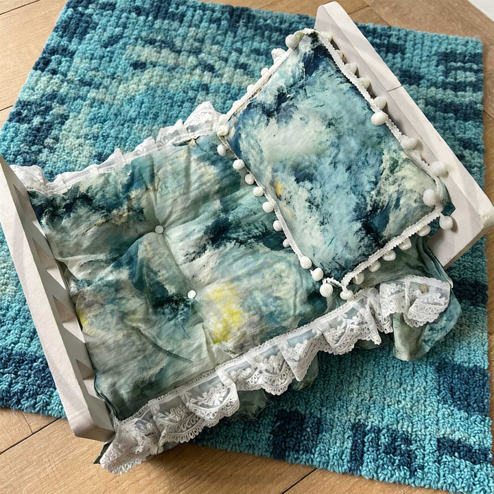 A 2-piece set featuring a newborn blanket and pillow with blue tie-dye and pom pom trim for newborn photography.