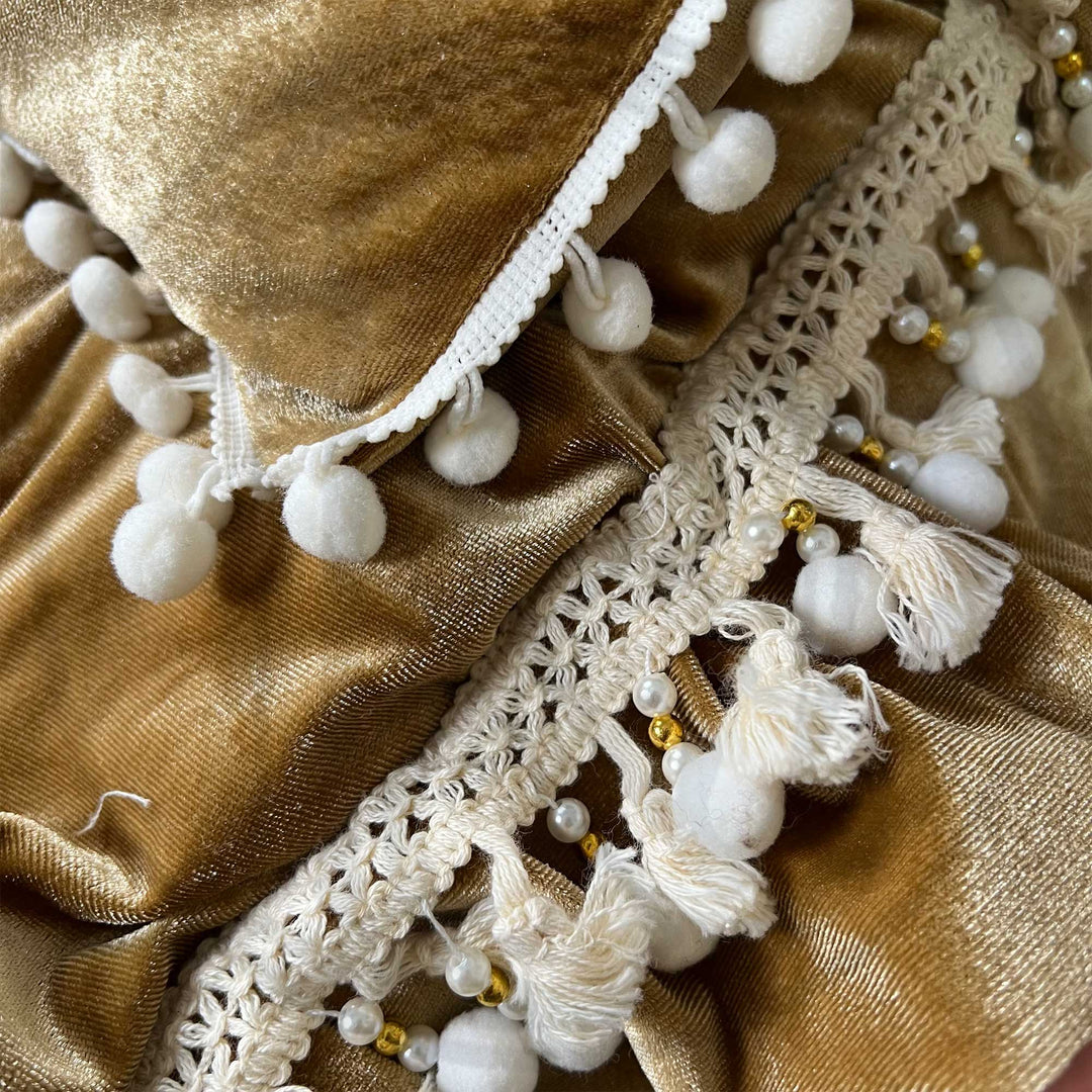 A close-up view of a camel velvet tufted pillow featuring ruffled pom-pom trim.