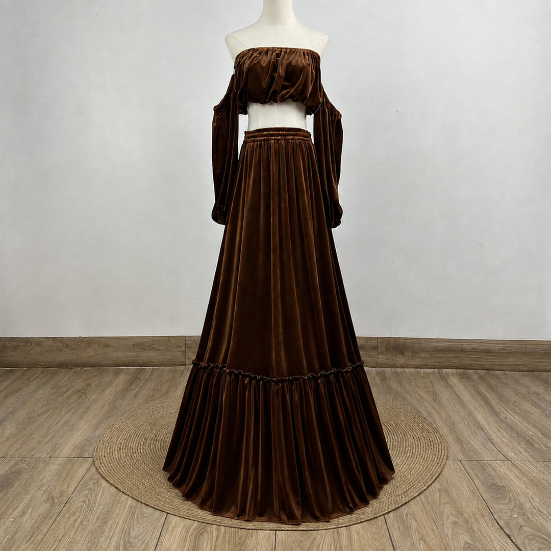 A dark brown velvet off-the-shoulder maxi dress displayed on a white mannequin, set against a neutral gray wall and light wood floor.