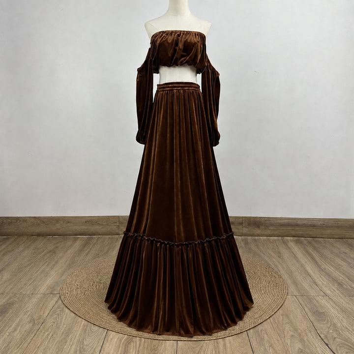 A dark brown velvet off-the-shoulder maxi dress displayed on a white mannequin, set against a neutral gray wall and light wood floor.