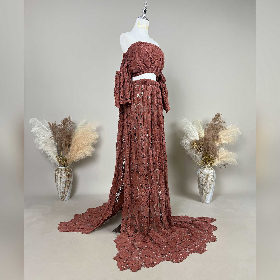 A terracotta two-piece lace maternity set displayed on a mannequin, featuring an off the shoulder ruffled crop top and a high waisted floor length skirt with a sweeping train.