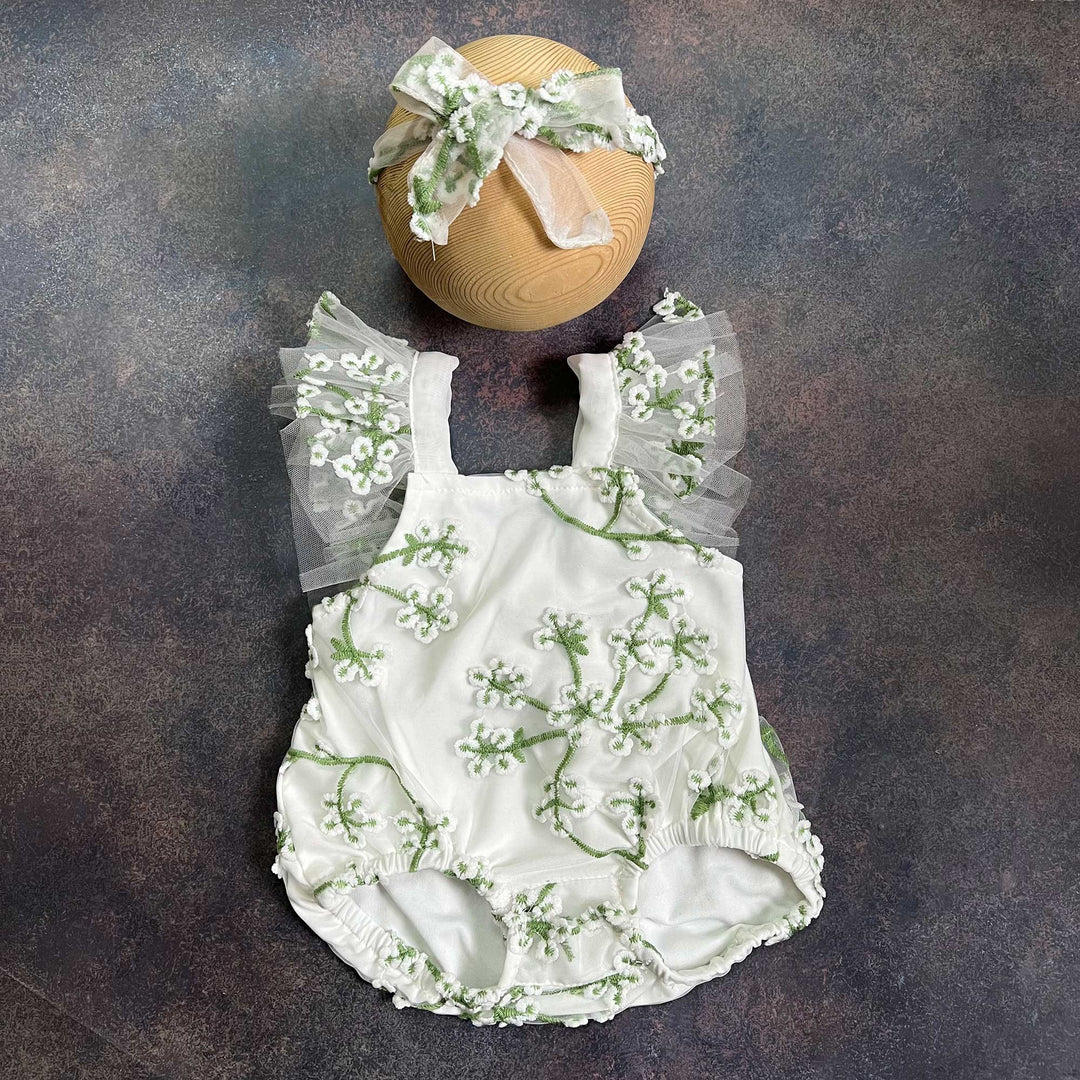 A romper laid flat from the front, showing the square neckline, tulle flower straps on both sides and gathered leg openings, with the same headband above.