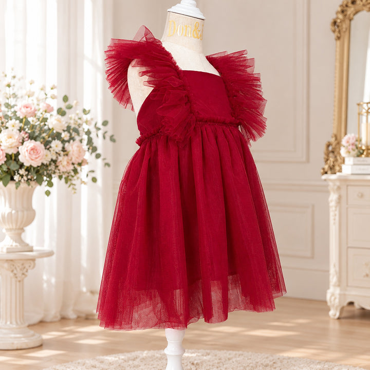 A Callisto red tulle dress on a mannequin with tulle ruffled shoulders; flowers and a mirror indoors.