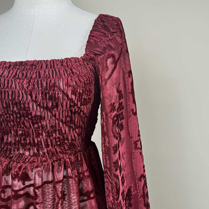 A close-up of the Calypso red wine dress on a mannequin, showing the square neckline, smocked bodice and patterned long sleeve.