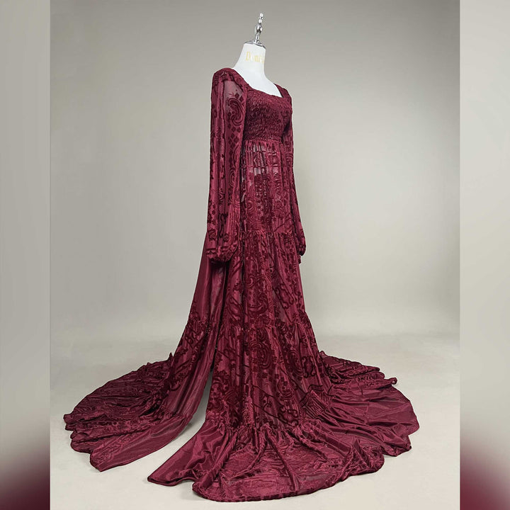 A Calypso red wine long-sleeve dress on a mannequin, shot from a side angle, with the train spread to both sides.