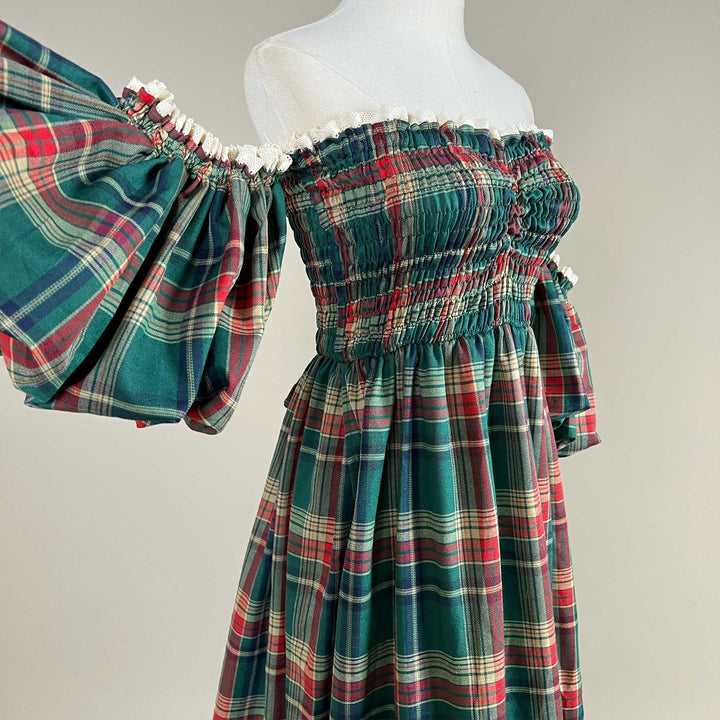 An oblique close-up of the Catubri plaid dress, showing one puff sleeve, the smocked bodice and the plaid skirt.