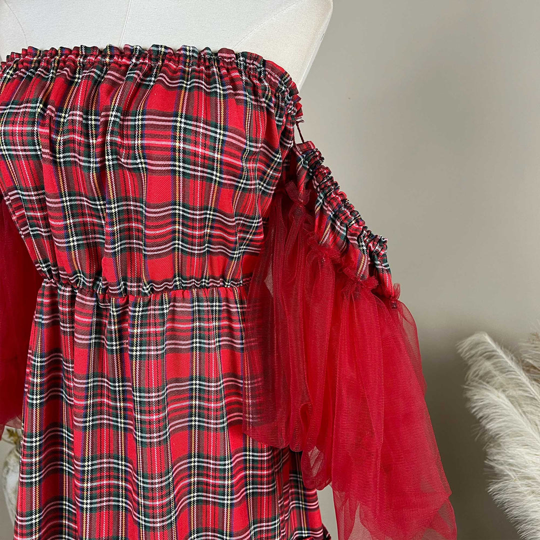 A close-up of the Celaeno plaid dress, showing the plaid fabric, gathered sleeve and red tulle sleeve, with a feather decoration at the lower right.