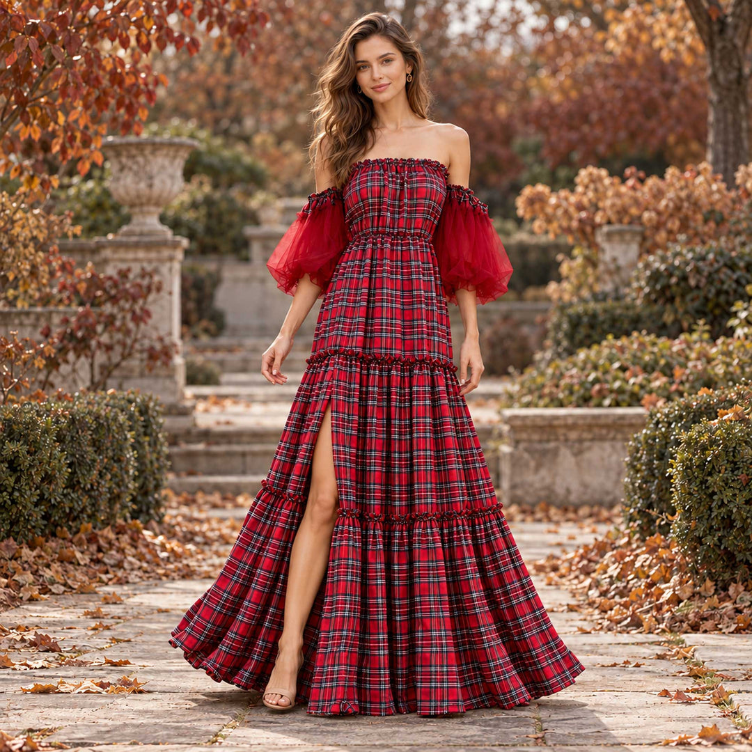 A woman in the Celaeno plaid off-shoulder dress with sandals stands on a stone path with fallen leaves, shrubs and a stone balustrade on both sides.
