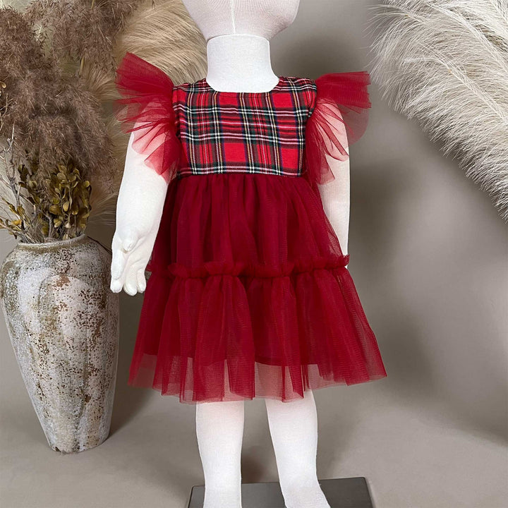 A Cerridwen dress on a child mannequin with white tights, a vase with dried flowers on the left and feather decoration on the right.