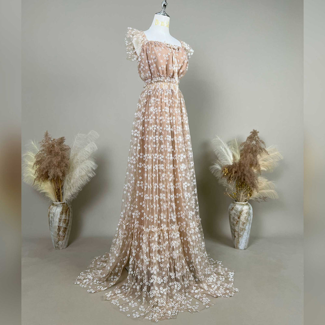 A khaki tulle gown with intricate white floral embroidery is displayed on a mannequin against a neutral gray studio background