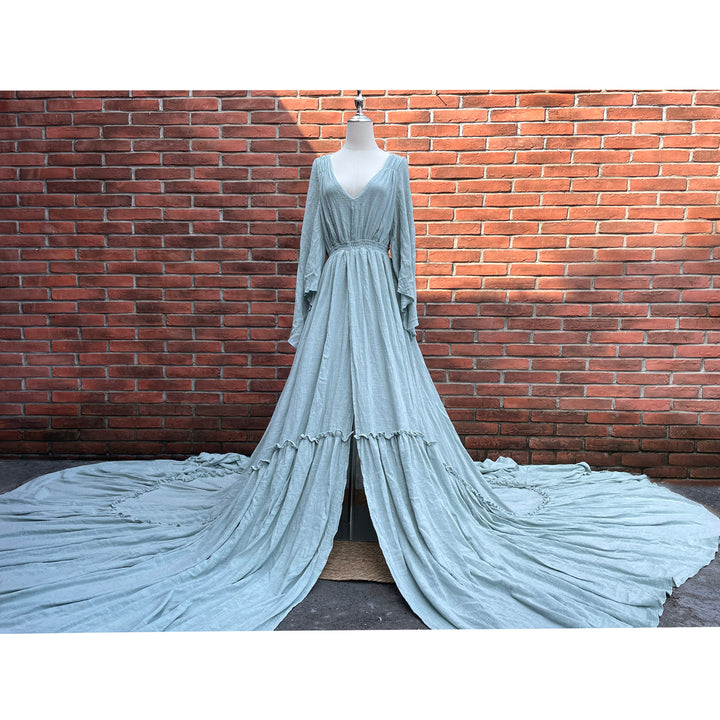 A light blue long-sleeved V-neck gown is displayed on a mannequin.The dress features a high front slit and its hem and train are spread out on the wooden floor.