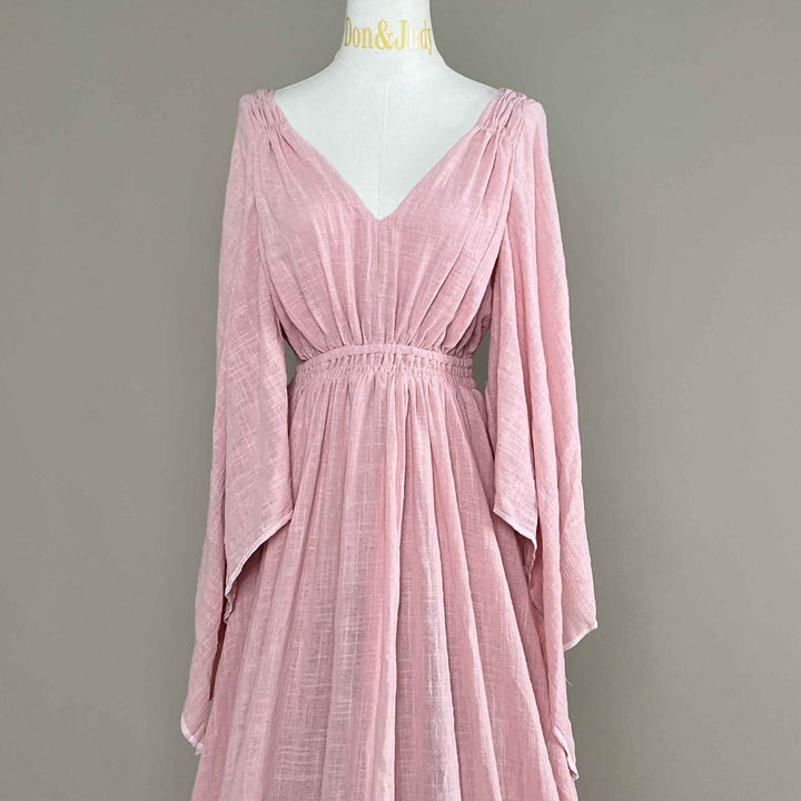 A Daphne Pink long-sleeved V-neck gown is displayed on a mannequin.The dress features a high front slit and its hem and train are spread out on the wooden floor.