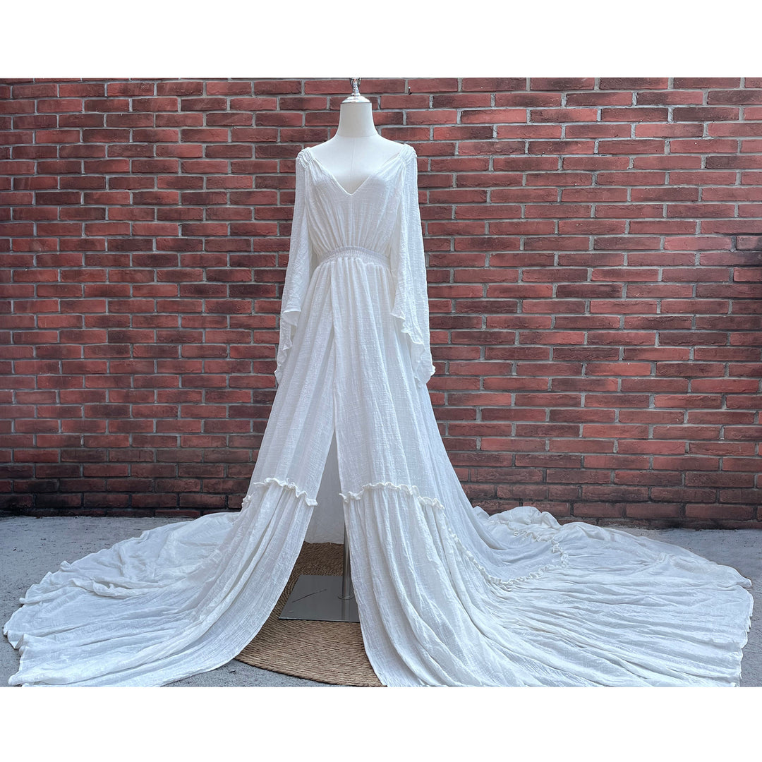 A Daphne ivory long-sleeved V-neck gown is displayed on a mannequin, with hands positioned on the simulated belly. The dress features a high front slit and its hem and train are spread out on the wooden floor.

