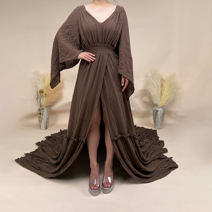 A Daphne coffee long-sleeved V-neck gown is displayed on a mannequin. The dress features a high front slit and its hem and train are spread out on the wooden floor.

