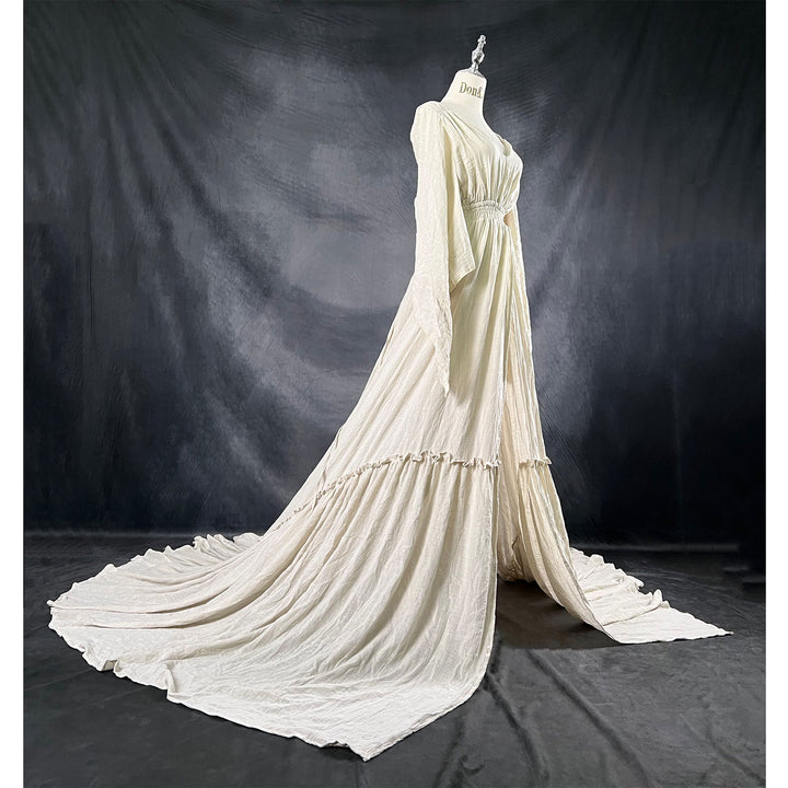 A Daphne light grey long-sleeved V-neck gown is displayed on a mannequin, with hands positioned on the simulated belly. The dress features a high front slit and its hem and train are spread out on the wooden floor.