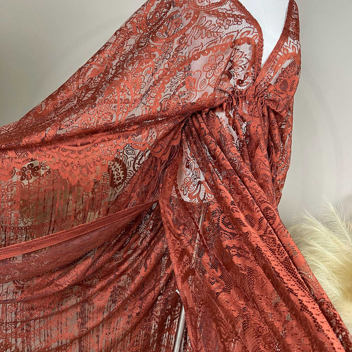 A mannequin displays a close-up of a rust lace cape featuring floral openwork texture and a deep V-neck; the fabric is semi-transparent mesh.