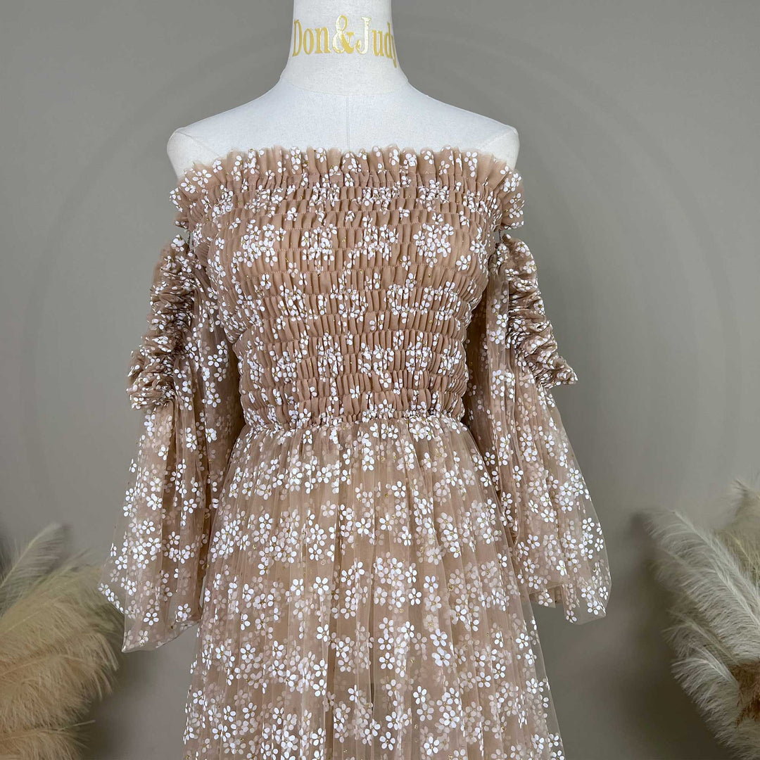 A khaki tulle dress with floral embroidery is displayed on a white mannequin torso. The dress features an off-the-shoulder neckline with shirred bodice detailing, long sleeves with gathered cuffs.