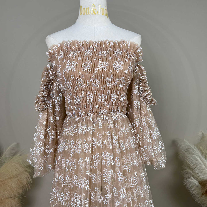 A khaki tulle dress with floral embroidery is displayed on a white mannequin torso. The dress features an off-the-shoulder neckline with shirred bodice detailing, long sleeves with gathered cuffs.