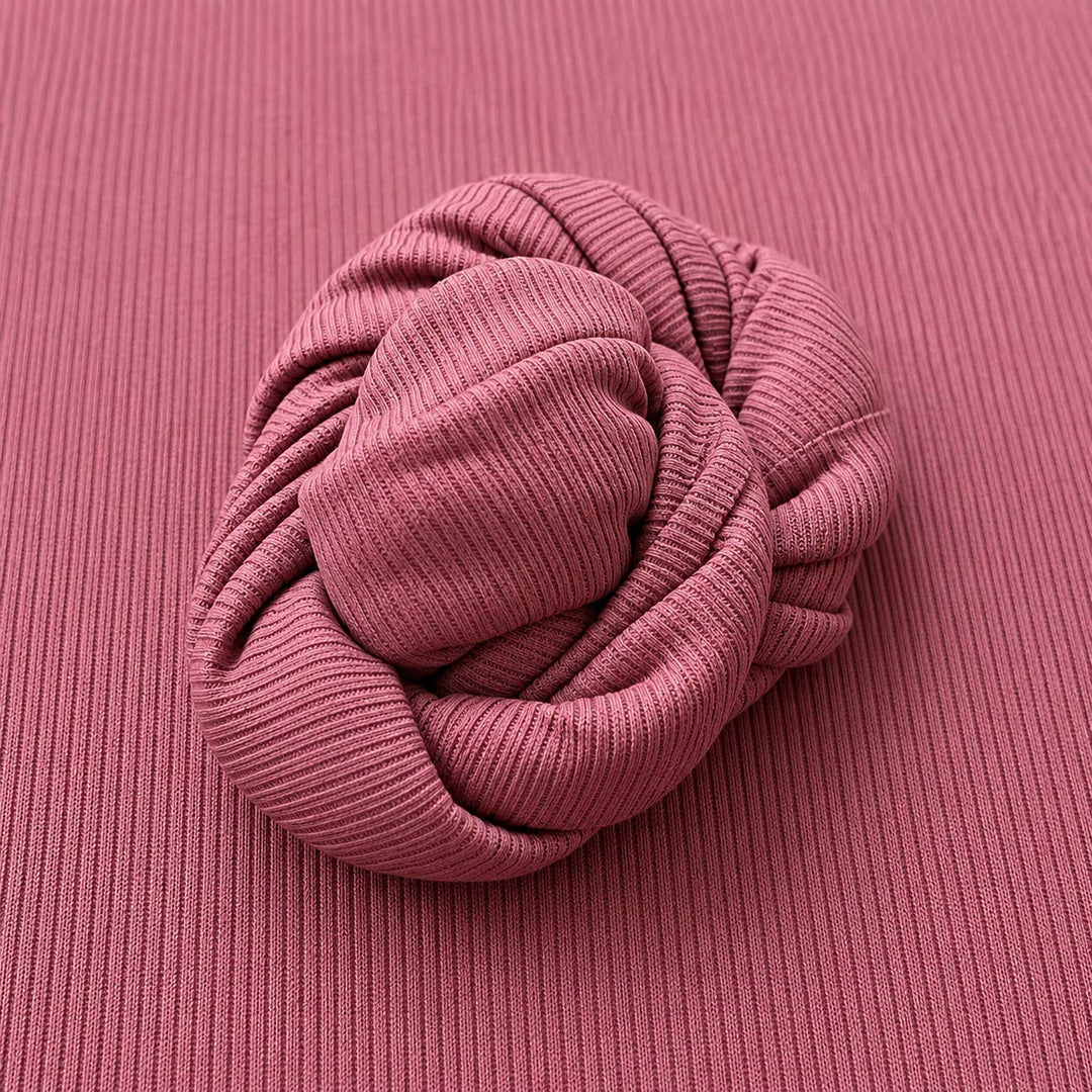 A mauve ribbed knit fabric fills the frame, with a strip of the same fabric rolled into a spiral at the center.