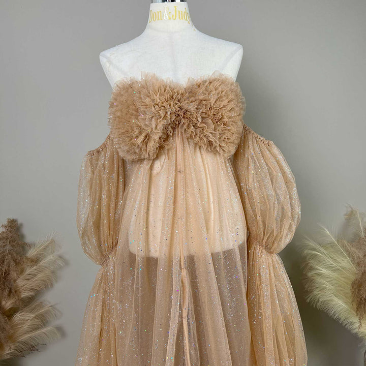 A mannequin displays the upper body of a khaki sequined off-shoulder gown with ruffled chest decor and puff sleeves; the dress is covered in sequined tulle.