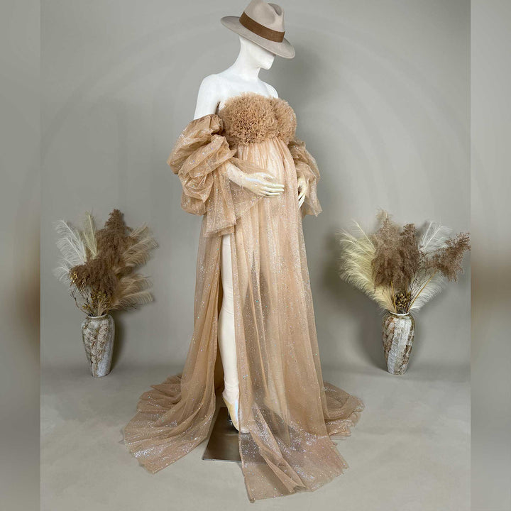 A hat-wearing mannequin displays a champagne sequined off-shoulder maternity gown with feather chest decor and a split train.