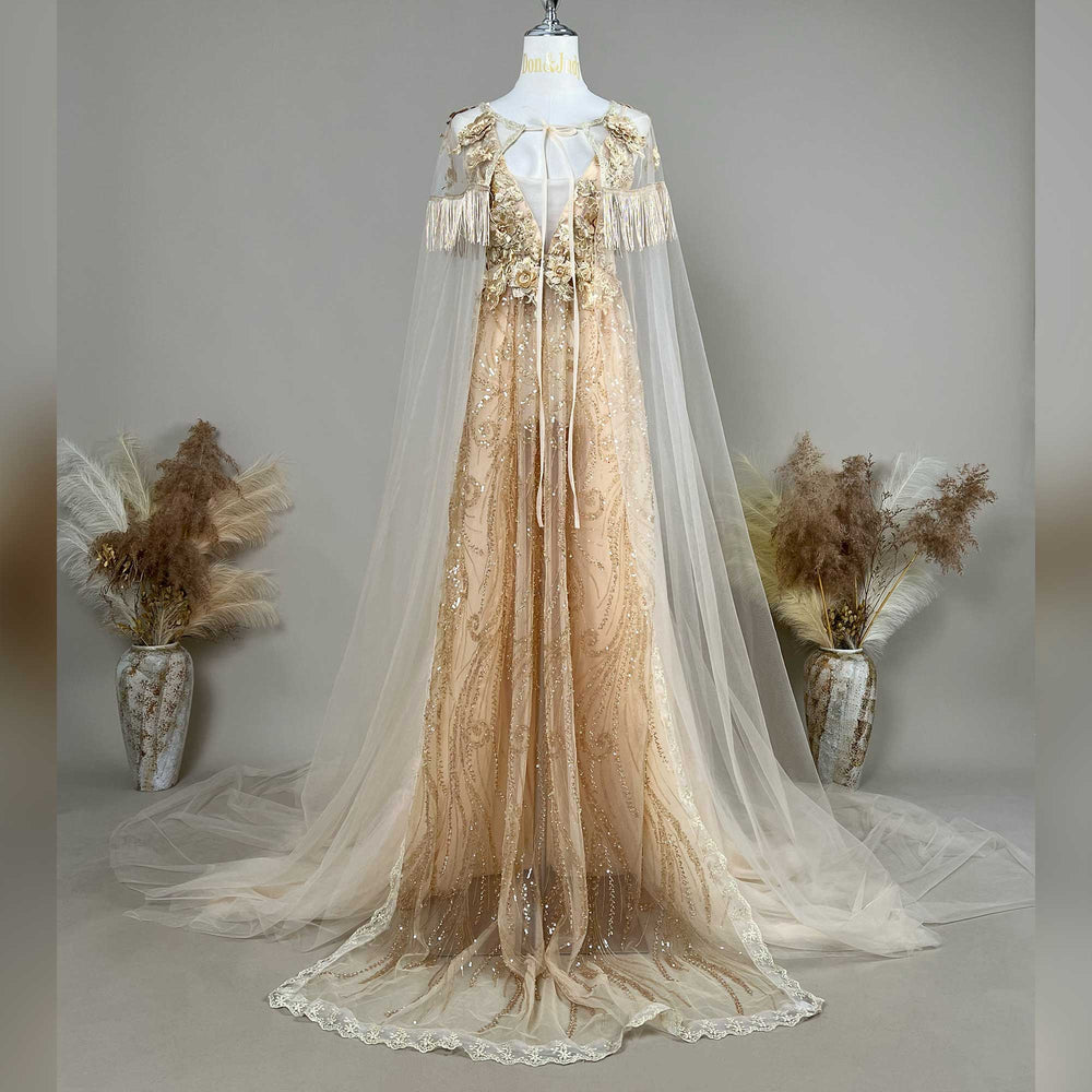 A gold sequined gown with a tulle cape is displayed on a mannequin, featuring fringe cuffs and a train skirt.