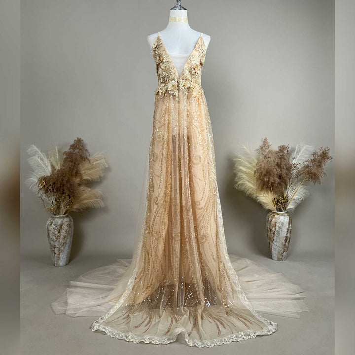 A mannequin displays a gold spaghetti strap gown with a deep V-neck, 3D floral decorations, and a train skirt.