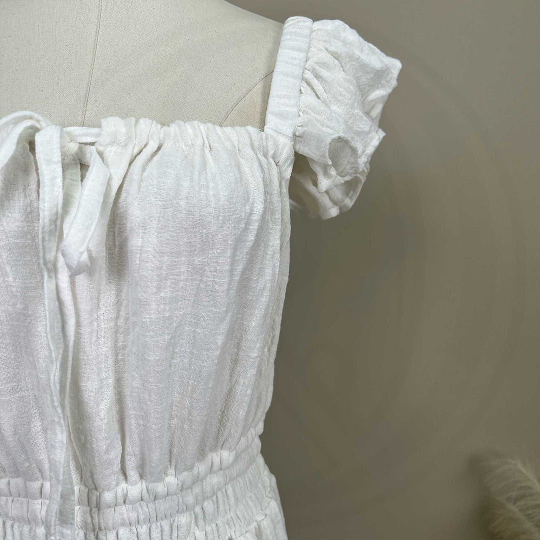 A ivory Tethys gown is displayed on a mannequin, featuring ruffled short sleeves, a front tie, and an elasticated waist.